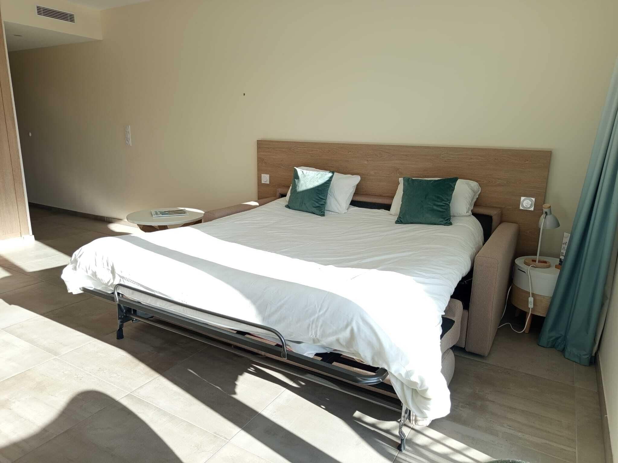 Una habitación de hotel con una cama grande, dos mesitas de noche y una ventana con cortinas.