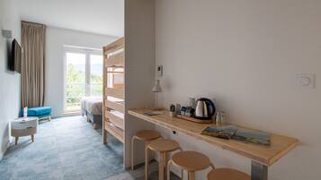 Una habitación de hotel moderna con un escritorio de madera, dos taburetes, una cama, un televisor y vistas al exterior.