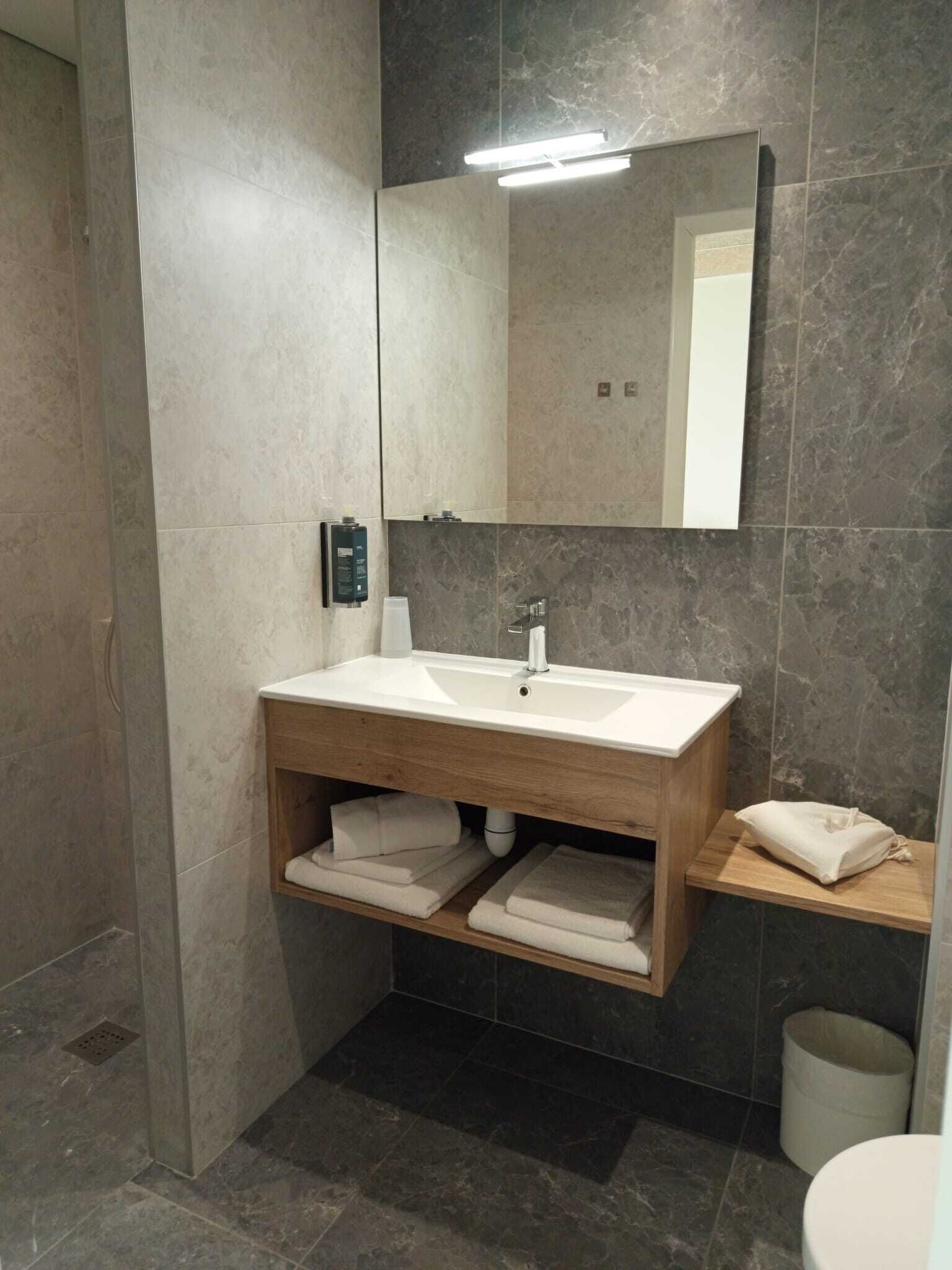 Un baño moderno con tocador de madera, un espejo grande y pared con azulejos oscuros.
