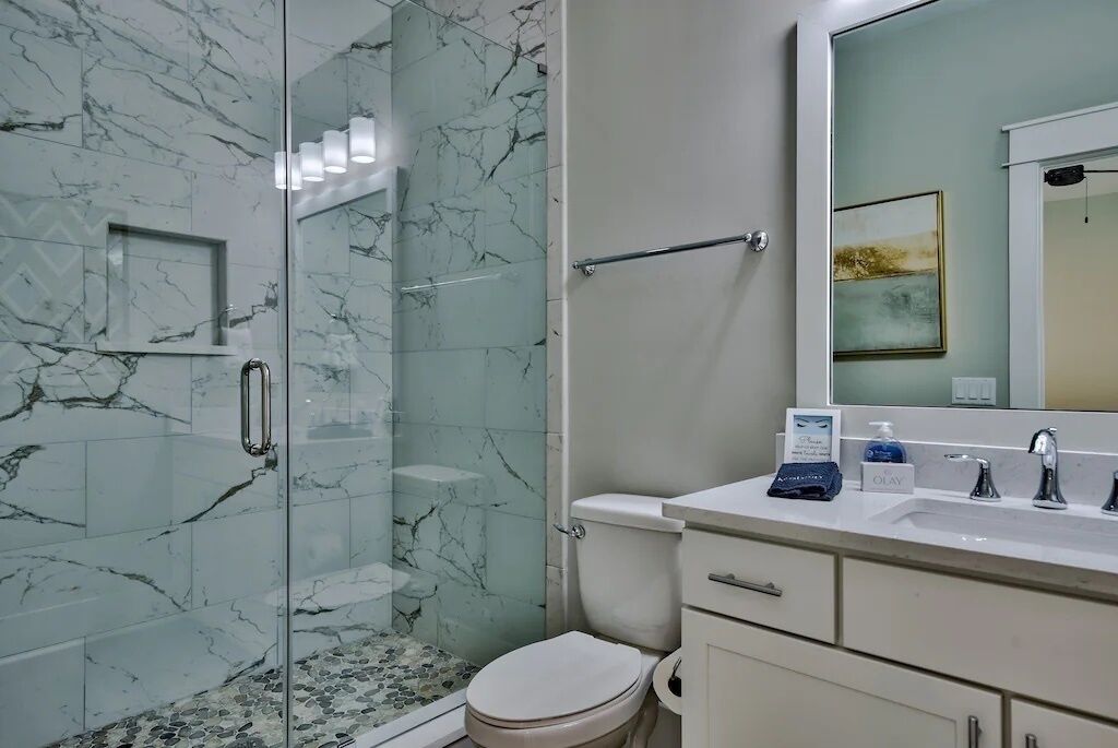 A modern bathroom with a glass-enclosed shower, marble walls, a white toilet, and a vanity with a mirror and sink.