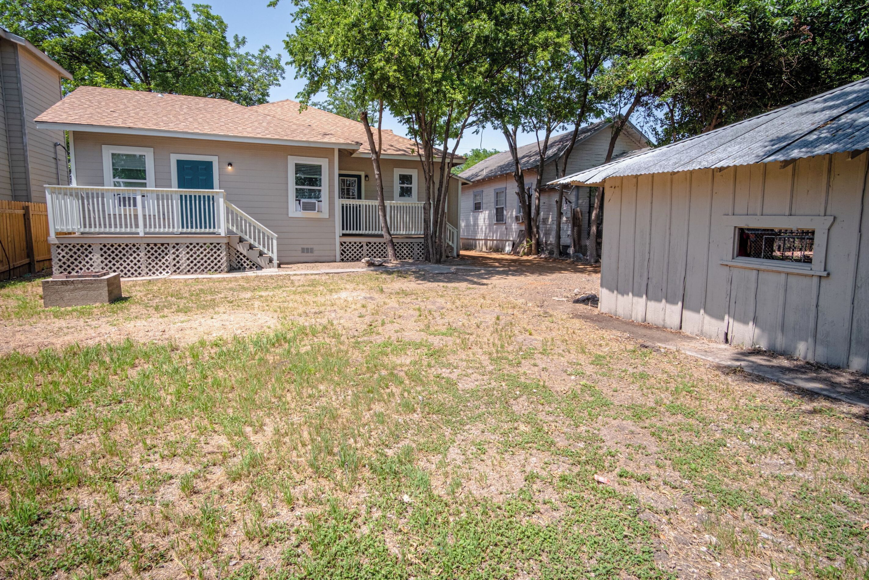 A residential area with a house featuring a front porch, a small deck, and a fenced yard.
