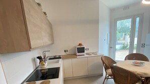 Een compacte keuken met een fornuis, magnetron en kleine koelkast. Er is een eethoek met een tafel en stoelen.