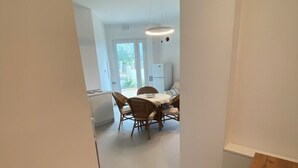 Een smalle gang die uitkomt in een eetgedeelte met een tafel en stoelen.