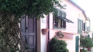 A pink building with a dark door, green shutters, and potted plants. - Apartment (Sant'Ilario)