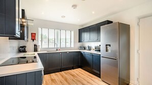 A modern kitchen with dark cabinets, a stainless steel refrigerator, and a window with blinds. - Oystercatcher (Stranraer)