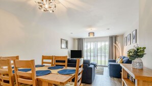 A modern living room with a dining area, wooden furniture, and large windows. - Oystercatcher (Stranraer)