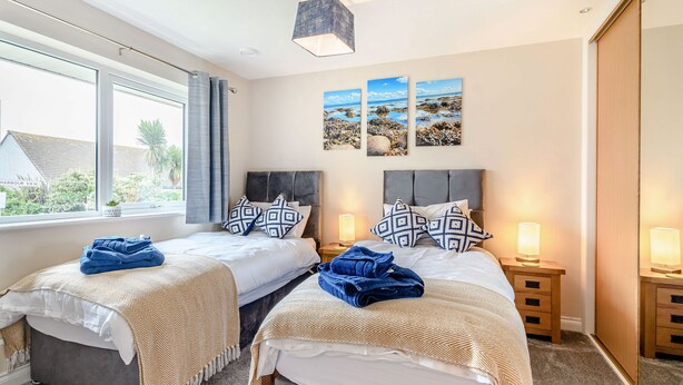A double room with two beds, each with a headboard, bedside tables with lamps, and a large window with curtains. - Oystercatcher (Stranraer)