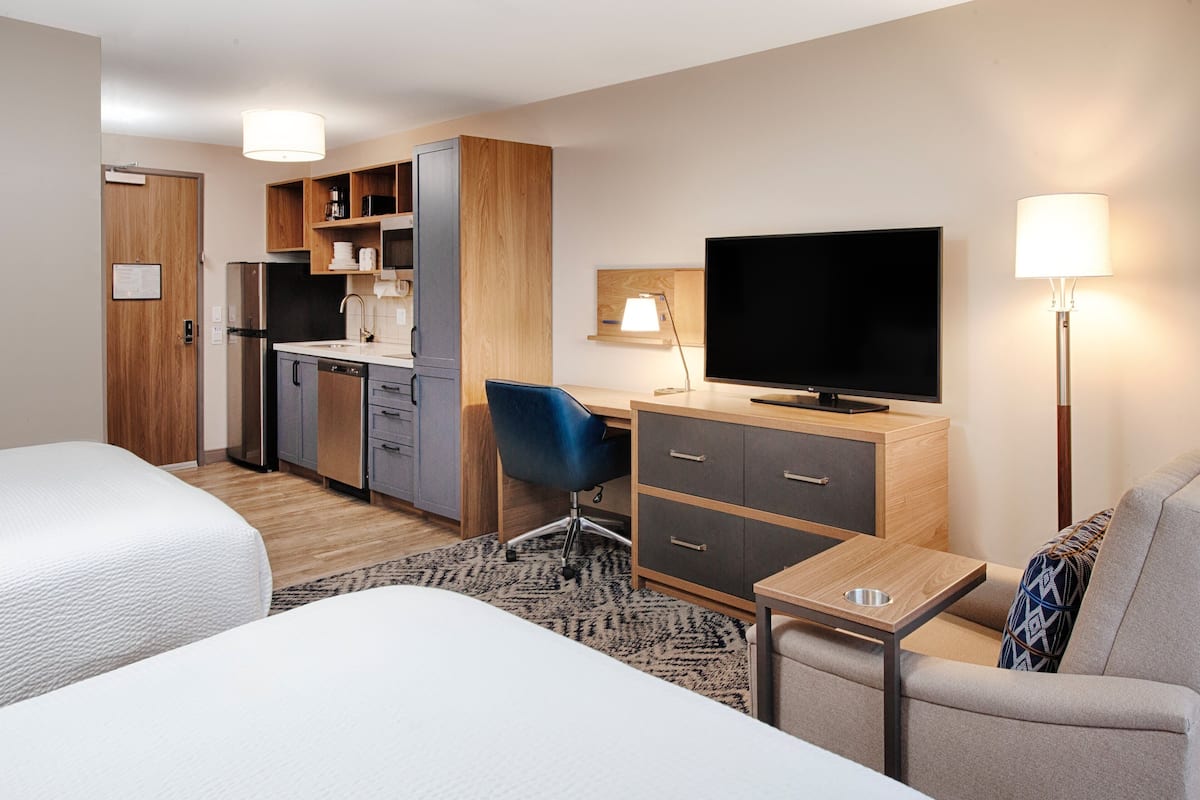 Une chambre d’hôtel avec deux lits, une kitchenette, un bureau avec une télévision et une lampe.