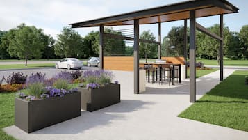Una zona de estar exterior moderna con un pabellón cubierto, macetas con flores y un sendero que la conecta.
