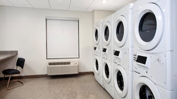 A laundry room with multiple stacked washing machines, a whiteboard, and a chair.