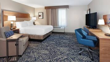 Una habitación de hotel con cama, escritorio, silla, televisión y aire acondicionado.