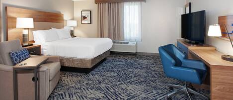 A hotel room with a bed, a desk, a chair, a TV, and an air conditioning unit.