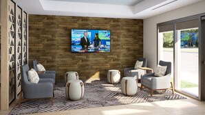 A modern living room with a large flat-screen TV mounted on a wooden wall, grey sofas with patterned cushions, and a patterned rug. - Candlewood Suites Detroit Sterling Heights by IHG (Macomb)