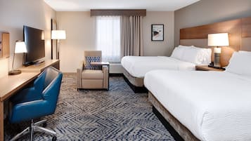 A hotel room with two beds, a desk with a TV, a chair, and a large window with curtains.