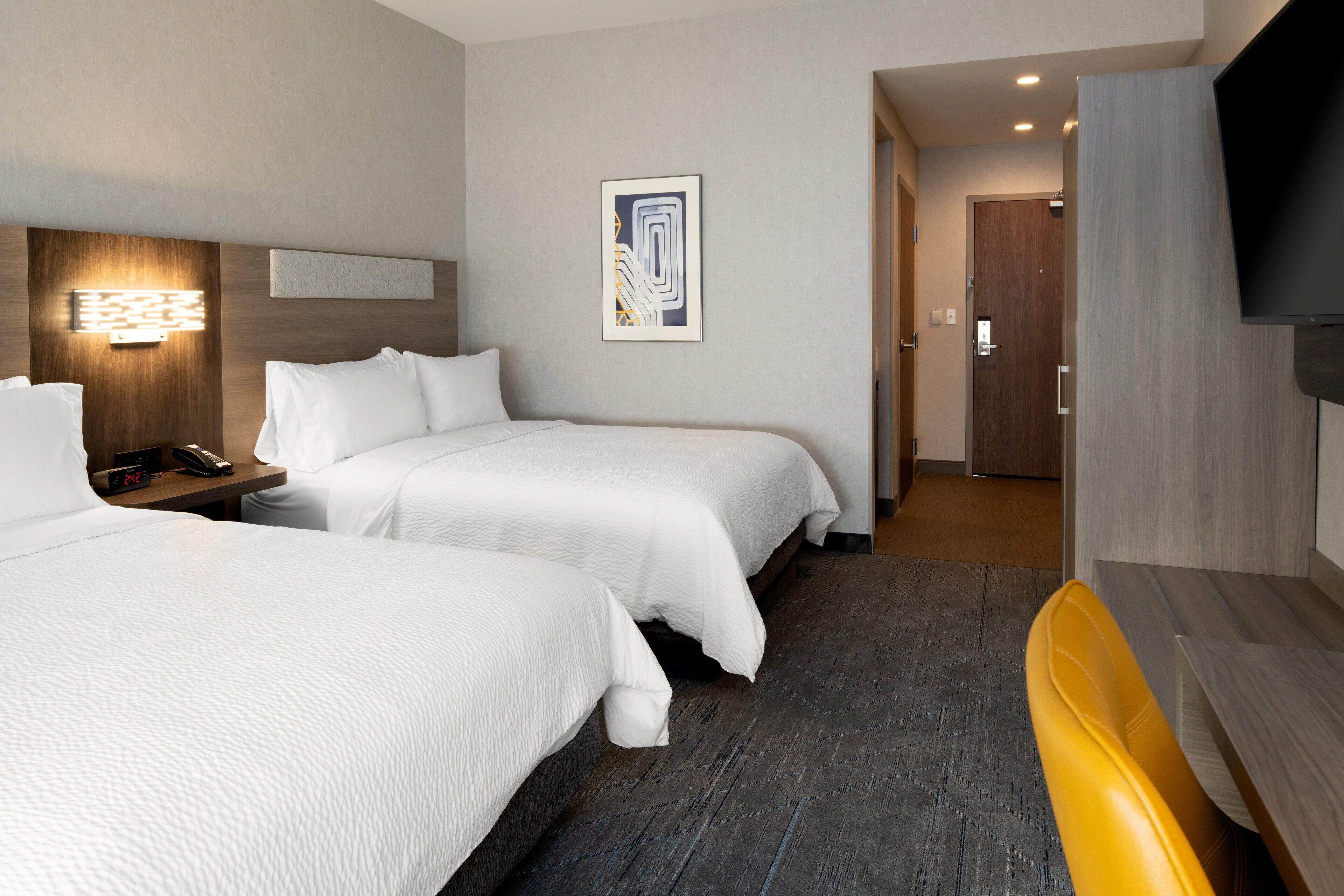 Ein Hotelzimmer mit zwei Betten, einem Nachttisch mit Telefon, einem an der Wand montierten Fernseher und einem gerahmten abstrakten Kunstwerk.