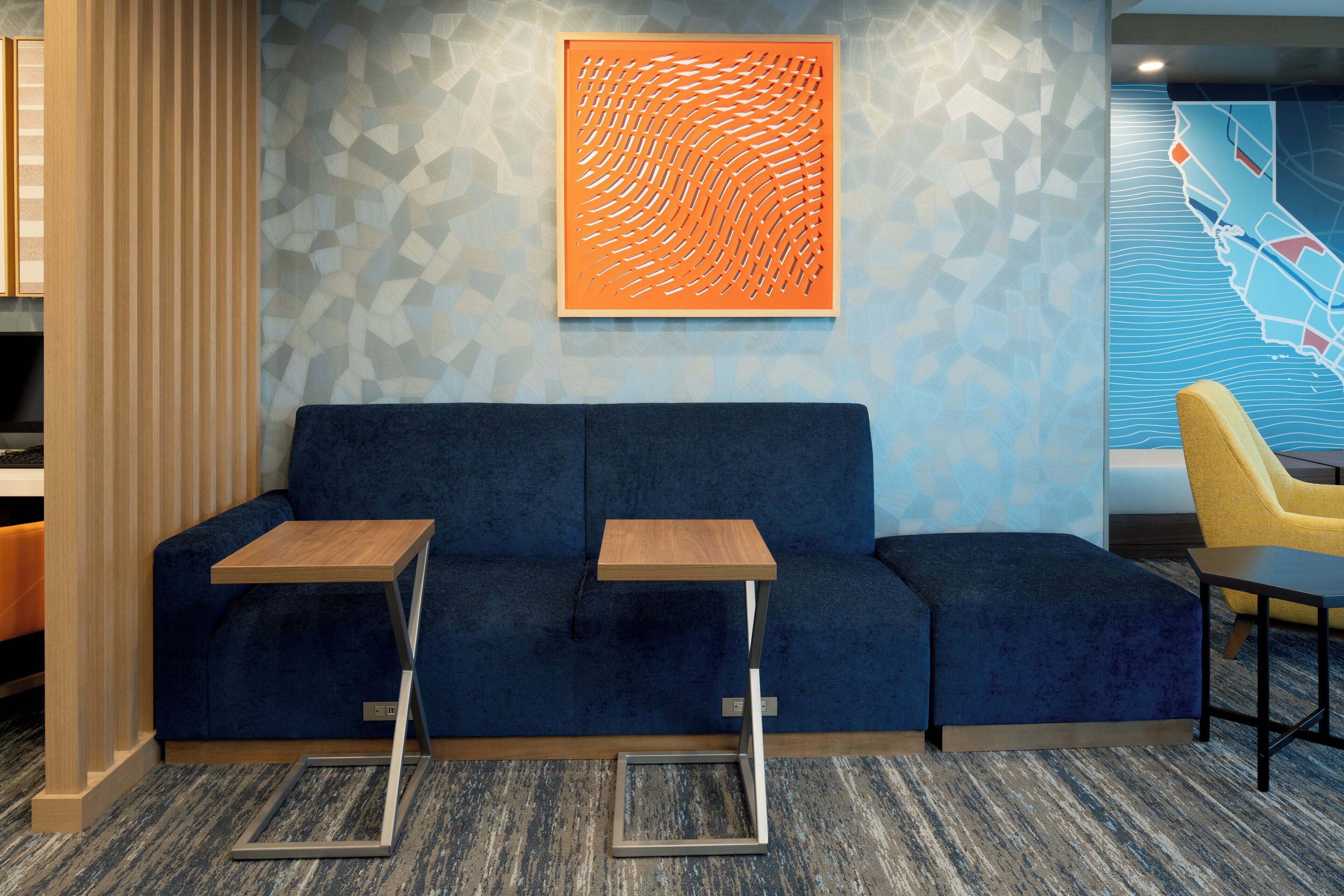 Un hall d’hôtel moderne avec un canapé bleu, deux petites tables en bois et une chaise jaune.