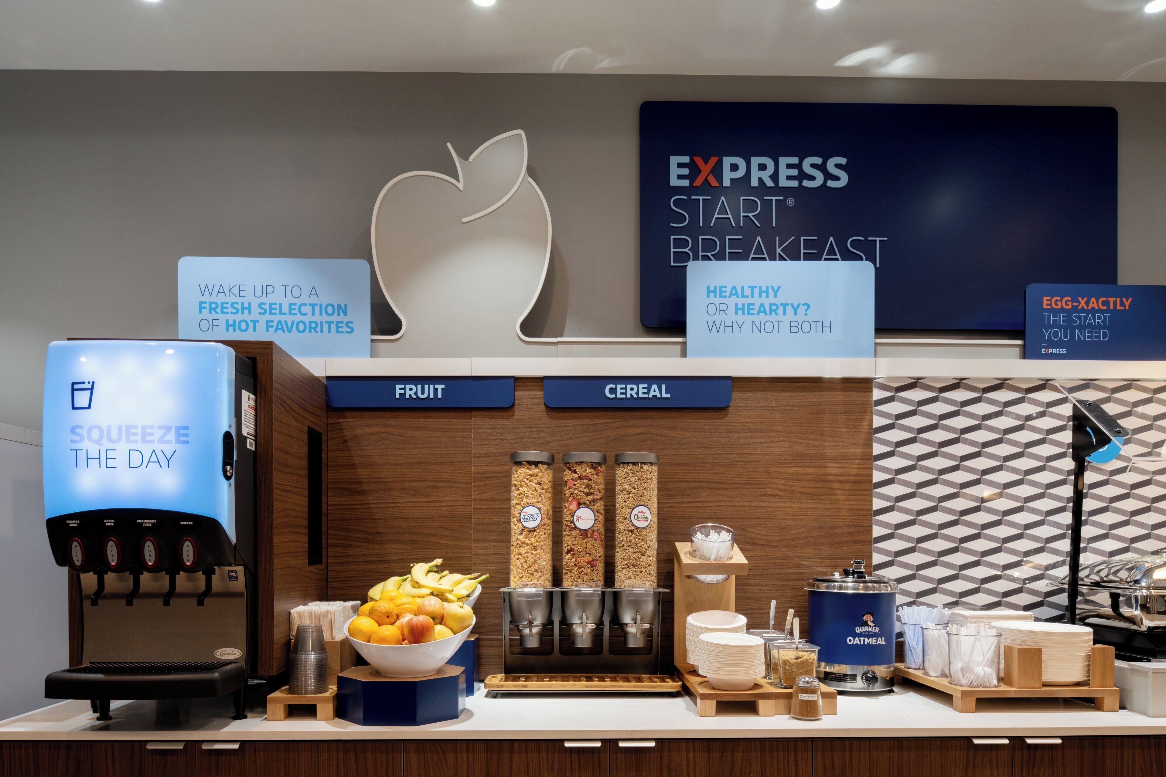 Uma estação de café da manhã com máquina de café, dispensadores de frutas e cereais, e uma tigela de frutas.