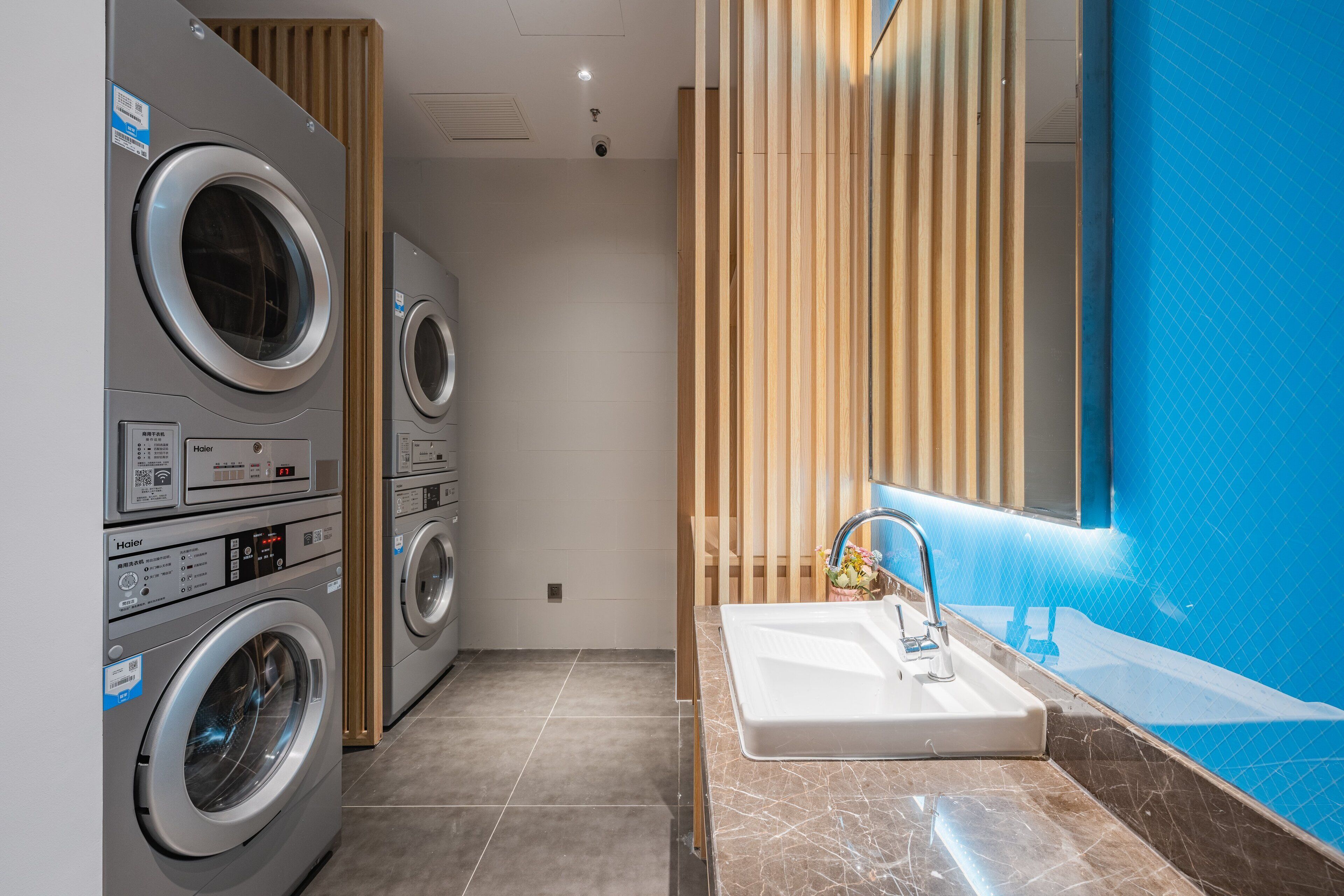 A laundry room with multiple washing machines and a sink with a blue-tiled wall.