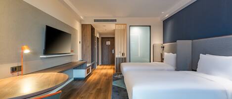 A modern hotel room with a large bed, a desk, a flat-screen TV, and a bathroom visible through a glass door.