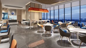 A modern dining area with a high ceiling, large windows, and a view of the cityscape.
