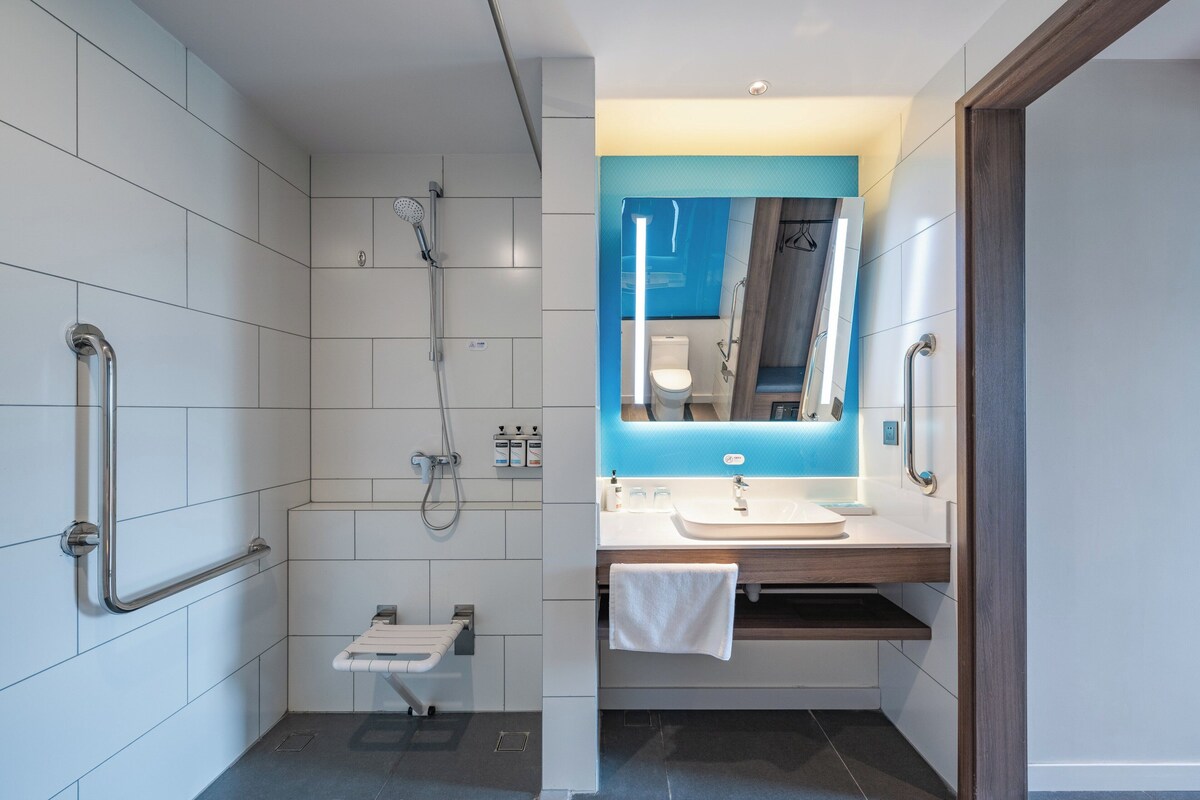 A modern bathroom with white tiles, a shower with a handheld showerhead, a sink with a mirror, and a towel rack.