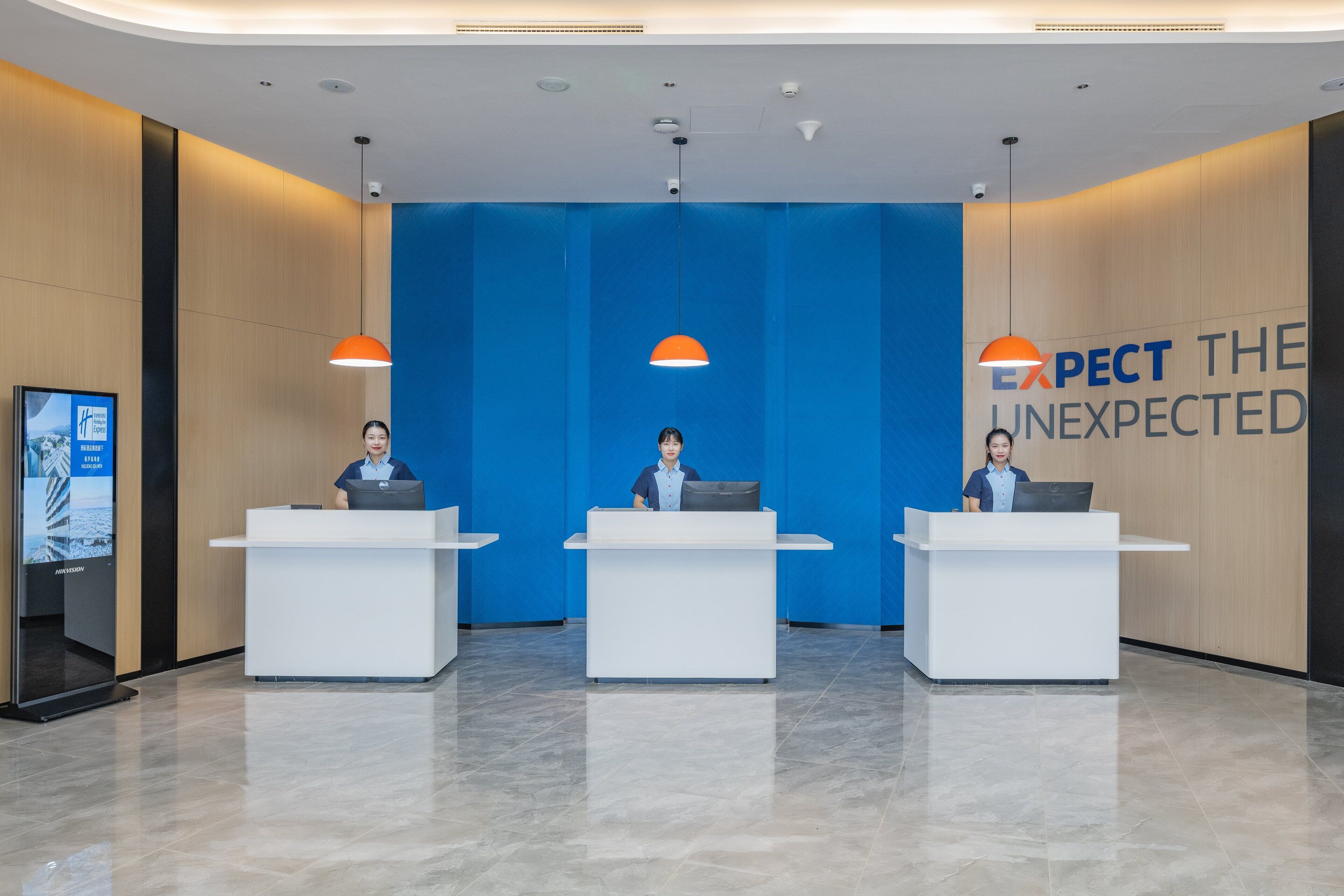 Zona de recepción con tres mostradores, una pared azul con el texto 'EXPECT THE UNEXPECTED' e iluminación colgante.