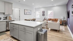 A modern kitchen with grey cabinets, a central island, and a dining area with a sofa and chairs. - 1/2 Block from King Street, Elegant Old Town Oasis ~ King Bed♛ ~ Free Parking (Alexandria)