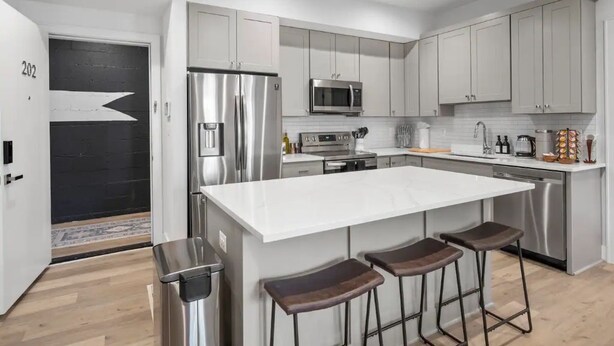 A modern kitchen with stainless steel appliances, a large island with bar stools, and light grey cabinetry. - 1/2 Block from King Street, Elegant Old Town Oasis ~ King Bed♛ ~ Free Parking (Alexandria)