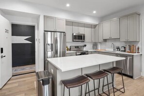 A modern kitchen with stainless steel appliances, a large island with bar stools, and light grey cabinetry. - 1/2 Block from King Street, Elegant Old Town Oasis ~ King Bed♛ ~ Free Parking (Alexandria)