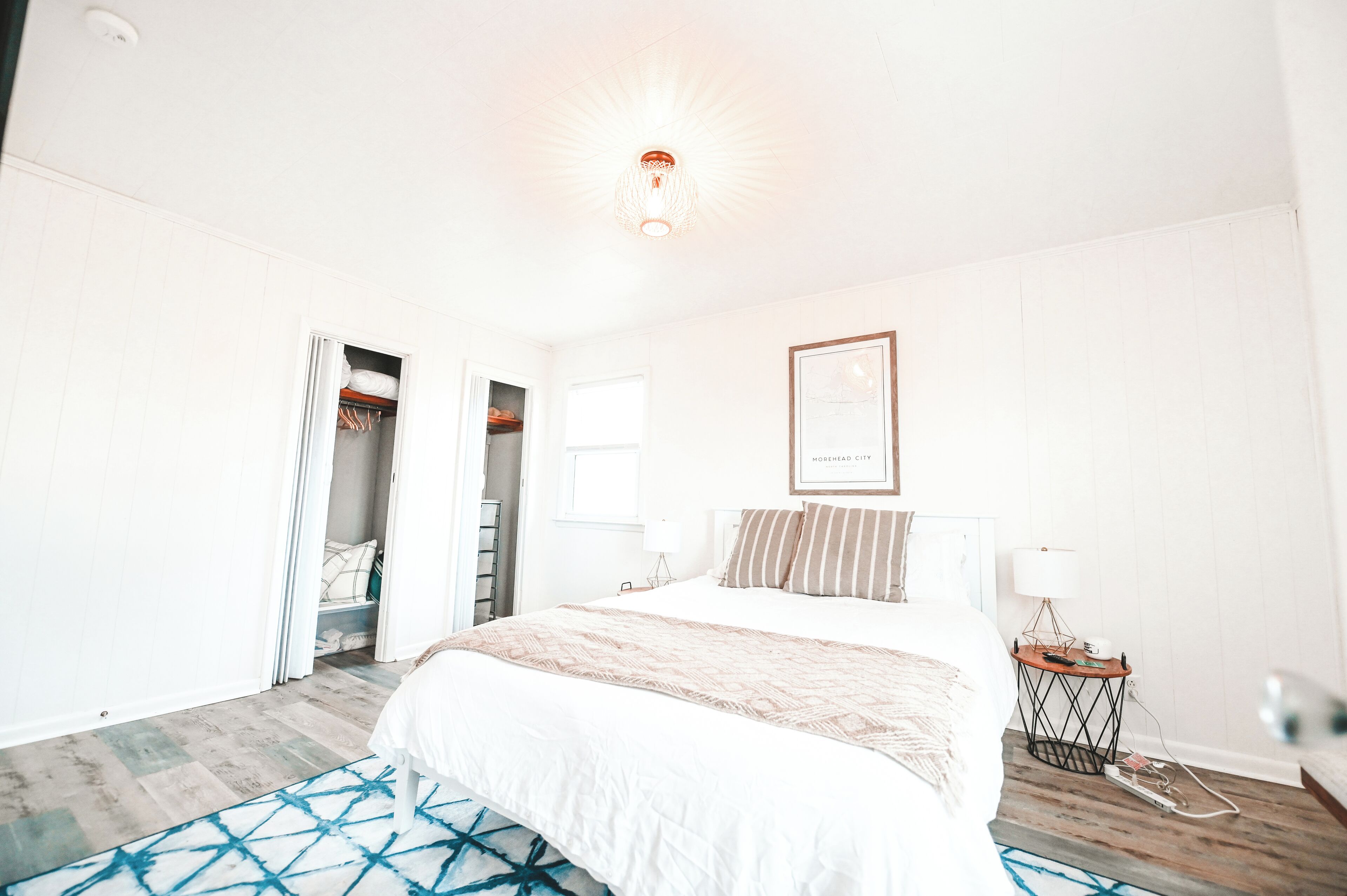 A hotel room with a bed, a bedside table, a lamp, and a framed picture on the wall.