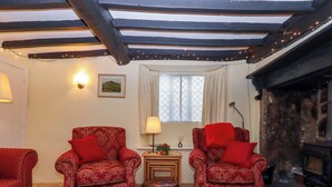 Uma sala de estar acolhedora com dois poltronas vermelhas, uma mesa de madeira pequena, um tapete estampado e uma lareira.