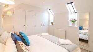 Quarto com uma cama grande, um guarda-roupa, um radiador, uma janela com vista e um espelho refletindo a cama.
