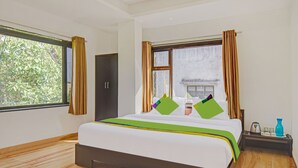 A hotel room with a large bed, a wardrobe, a window with curtains, and a nightstand with a kettle and a vase. - Treebo Villa Inn Aurangabad (Chhatrapati Sambhajinagar)
