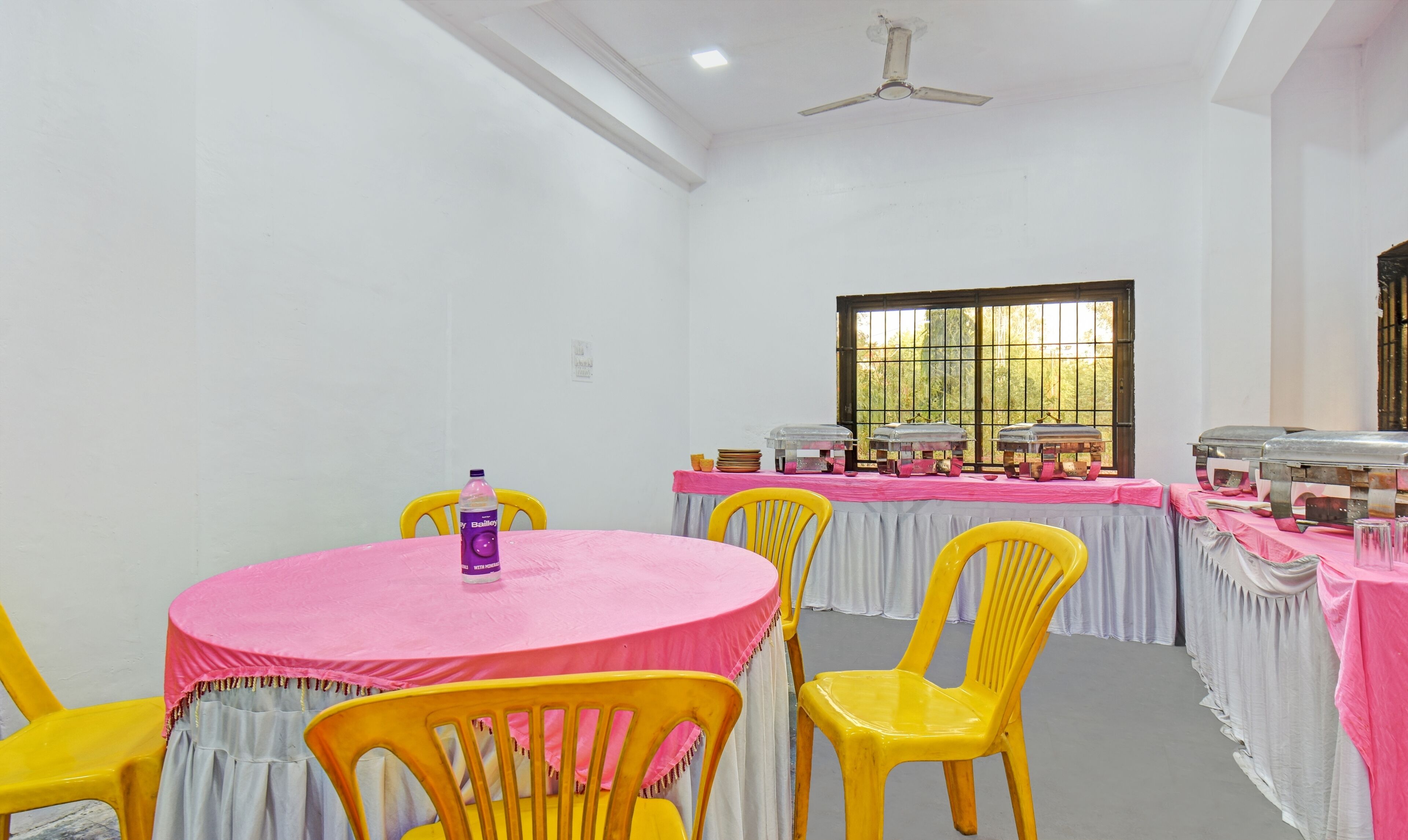A conference room with a round table, yellow chairs, a ceiling fan, and buffet-style food service.