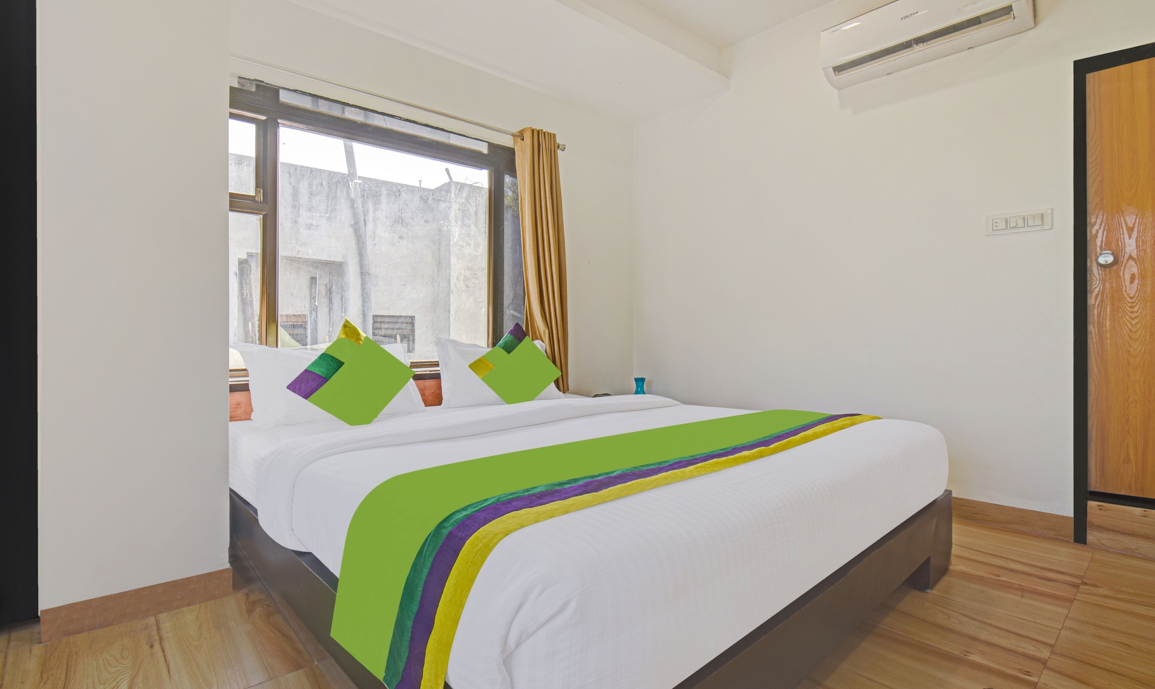 Een hotelkamer met een groot bed, een raam met gordijnen, een airconditioning en een houten deur.