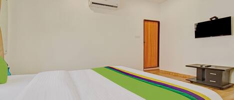 A bedroom with a bed, an air conditioning unit, a wooden door, a TV, and a small desk with drawers.