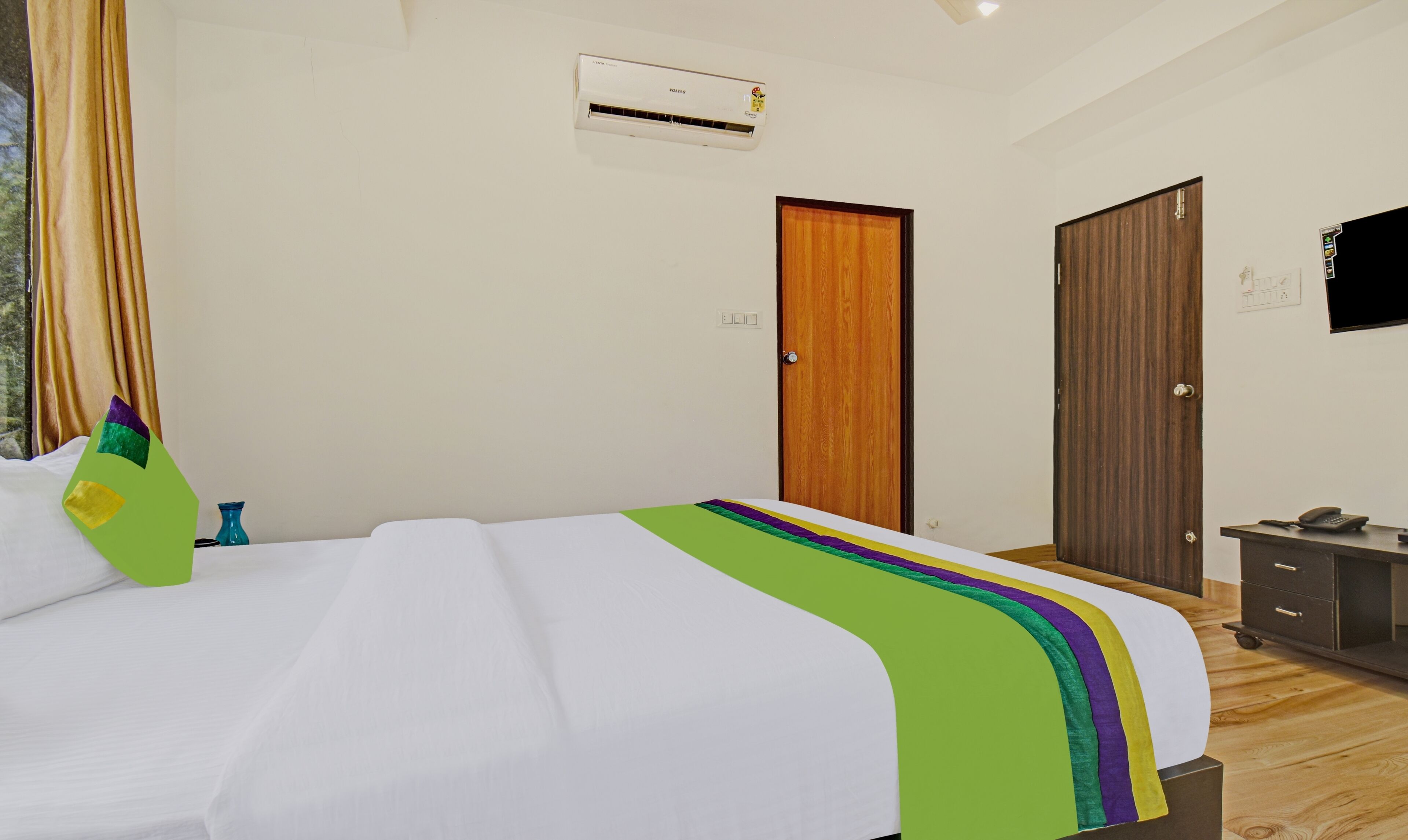 A hotel room with a bed, a desk, a wardrobe, and an air conditioning unit.