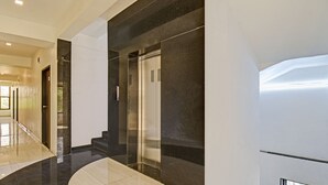 A modern hotel lobby with a marble floor, a glass elevator, and a staircase leading to an upper floor. - Treebo Villa Inn Aurangabad (Chhatrapati Sambhajinagar)