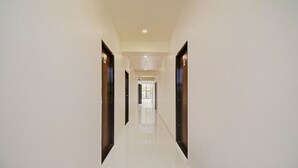 A long, narrow hallway with white walls and a shiny tiled floor, leading to a bright room with a large window. - Treebo Villa Inn Aurangabad (Chhatrapati Sambhajinagar)
