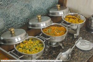 Montaje de bufé con diversos platos en recipientes metálicos, algunos con tapas.