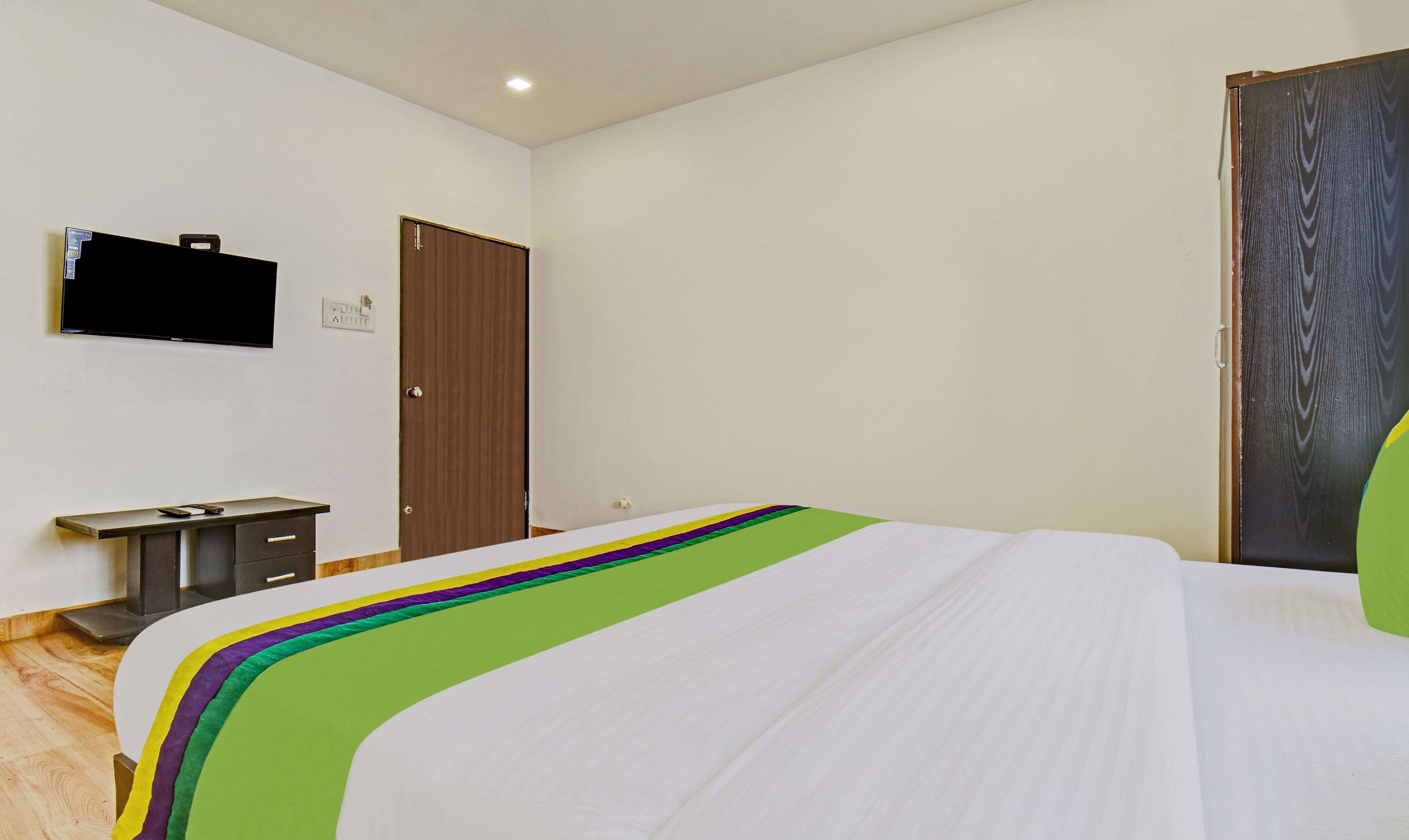 Un dormitorio con cama, televisor en la pared, escritorio con silla y armario.
