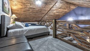 A bedroom with a sloped ceiling, a bed, a bench, and a view of the outside.