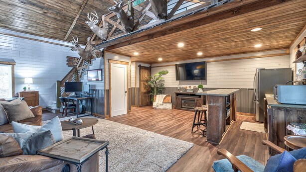 A rustic interior with a wooden ceiling, a dining area, a kitchen, and a living room with a sofa and coffee table.