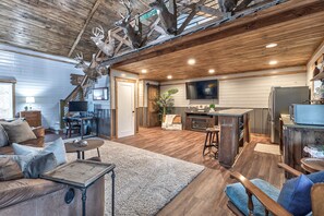 A rustic interior with a wooden ceiling, a dining area, a kitchen, and a living room with a sofa and coffee table.