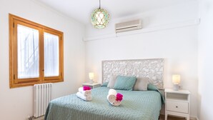 A neatly made bed with a green bedspread, two nightstands with lamps, a decorative headboard, and a window with blinds.