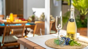 A table with a bottle of champagne and a glass on a woven placemat, with a dining area in the background.