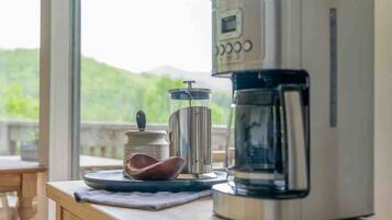 A coffee maker on a wooden table with a view of greenery and mountains in the background.