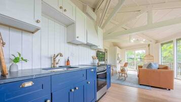 A modern kitchen with blue cabinets, a large island, and a view to a balcony with a sofa.