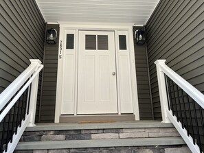 Enter through the double doors, flanked by lantern-style lights, to a welcoming entrance with a stone staircase.