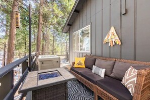 A cozy outdoor seating area with a wicker sofa, a fire pit, and a view of the forest.